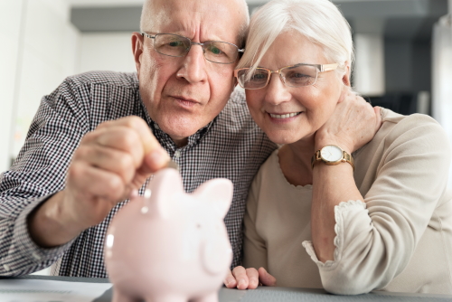 Senior couple puts the coin into the piggybank. Retirement savings concept.
